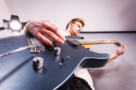 Young bearded man with electric guitar. Adult person is holding instrument and playing. Hobby, music...