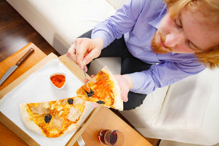 People, italian cuisine concept. Young bearded man eating hot fresh pizza adding tomato sauce. Delicious fast food meal.の写真素材