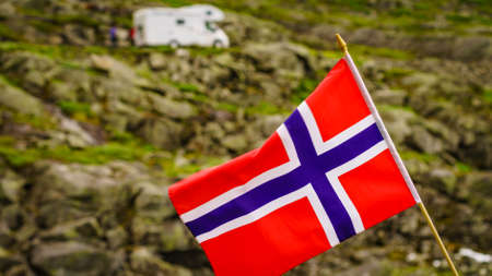 Norwegian flag waving on wind and camper car in mountains in the background. Travel, holidays and adventure concept.の写真素材