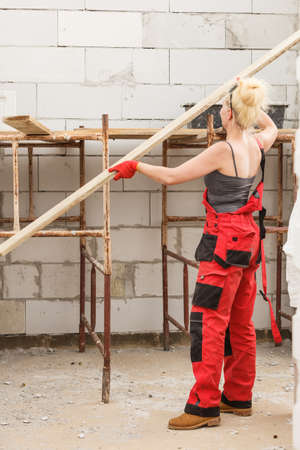 Strong woman in dungarees carrying big wooden plank board on her home construction site, building new home.の写真素材