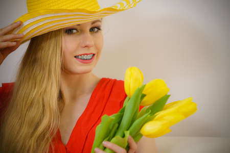 Lovely young woman long blonde hair summer hat on head sitting on couch holding yellow tulips.の写真素材