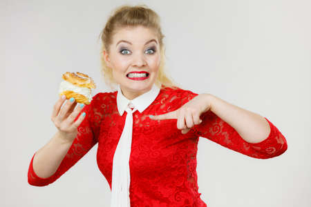 Skeptical woman holding choux puff with cream flavour having disgusted face expression being on...