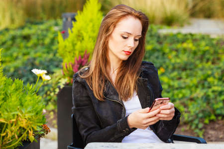 Woman sitting in urban relaxing place, waiting at table in outdoor restaurant cafe. Female looking at smart phoneの写真素材
