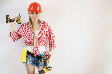 Woman wearing helmet using drill. Girl working at flat remodeling. Building, repair and renovation.の写真素材