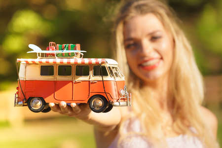 Happy woman having idea of traveling, holding hippie camper trailer decorative object model. Vehicle, summer vacations concept.の写真素材