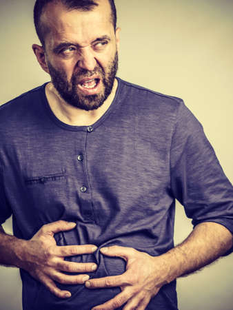Man having huge stomach pain holding his belly feeling very unwell. Guy being sick and unhealthy.の写真素材