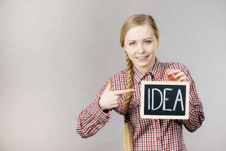Happy positive young woman holding idea sign banner on black board. Studio shot on grey.の写真素材