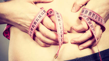 Getting rid of belly fat, diet, weight loss or gain concept. Woman touching stomach holding measuring tapeの写真素材