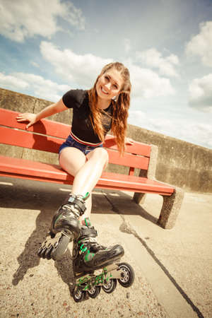 Happy joyful young woman wearing roller skates sitting on bench enjoying herself. Female being sporty having fun during summer time.の写真素材