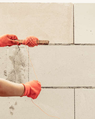 Woman builder using string as level in wall construction. Bricklayer, new house in progress.