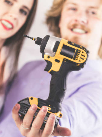Happy couple presenting small drill. Two people, man and woman showing renovation work tool gear.の写真素材