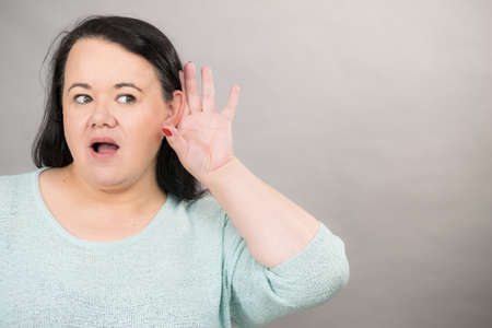 Gossip, rumors and hearing concept. Adult plus size woman round face putting hand to her ear to hear better.の写真素材