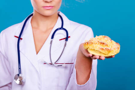 Serious dietitian nutritionist checking examine sweet roll bun with stethoscope. Woman with fattening junk food. Bad unhealthy eating nutrition concept.の写真素材