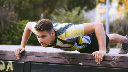 Young handsome man working out outdoor. Sporty guy flexing his muscles doing push ups.