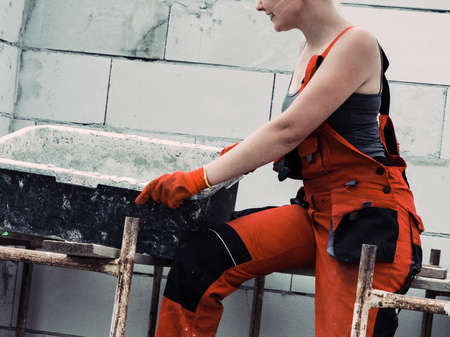 Woman wearing workwear working on construction site. Mixing cement in bowl preparing mortar. Partially built new home early stage. Industry.の写真素材