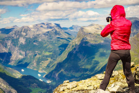 Tourism vacation and travel. Female tourist taking photo with camera, enjoying Geiranger fjord and mountains landscape from Dalsnibba Plateau viewpoint at windy day, Norway .の写真素材