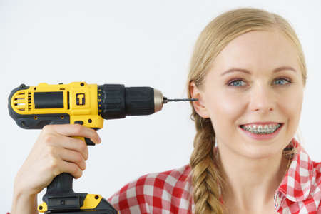 Funny cheerful woman pointing at her head or ear using drill. Crazy working female.の写真素材