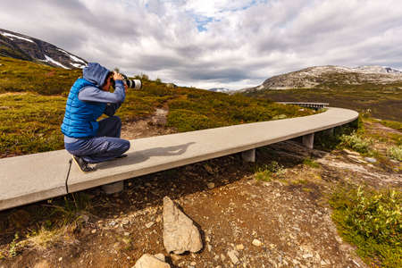 Woman with camera resting taking photo from Vedahaugane bench rest stop. National Tourist Route Aurlandsfjellet. Architecture Norway.の写真素材