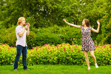 Happy funny hipster couple playing together blowing soap bubbles outdoor in spring park.の写真素材