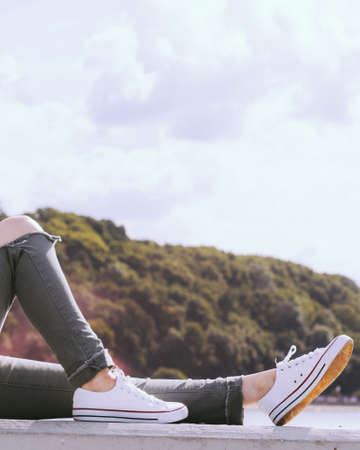 Trendy fashionable unrecognizable woman relaxing outdoor wearing casual footwear white sneakers and hole trousersの写真素材