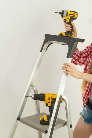 Woman fully equipped with work repairing tools about to stand on ladder. Female repairs indoor.の写真素材