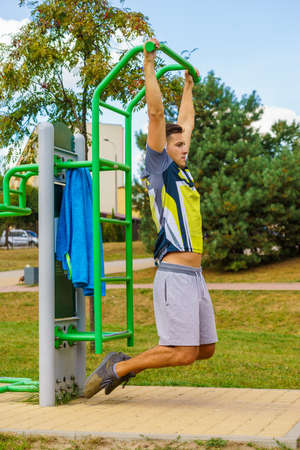 Young handsome man working out in outdoor gym. Sporty guy flexing his muscles doing pull ups on...