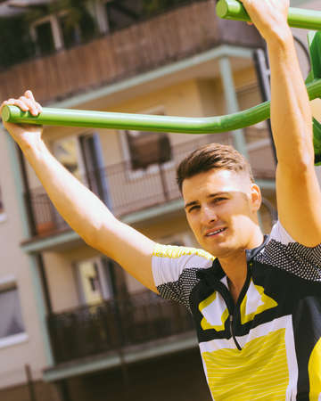 Young handsome man working out in outdoor gym. Sporty guy flexing his muscles on machine. Staying fit and healthy.の写真素材