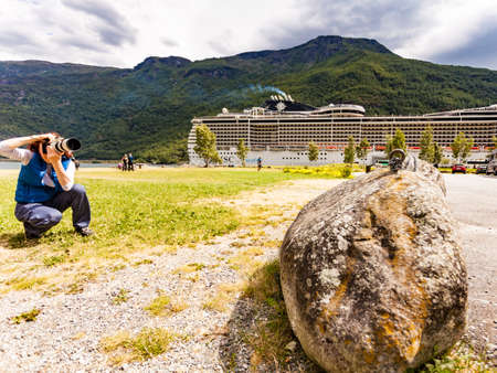 FLAM, NORWAY - JUNE 28, 2018: Woman with camera take photo and cruise ship MSC Preziosa on fjord Aurlandsfjord in norwegian tourist destination Flam village.のeditorial素材