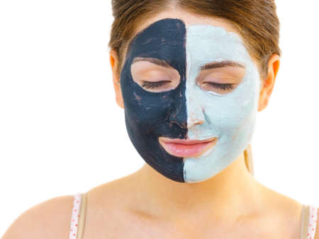 Woman with clay carbo black mask on half face and white mud on second half. Girl taking care of oily complexion. Beauty procedures. Skincare.の写真素材