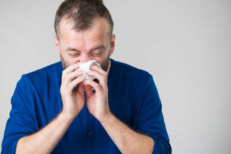 Man having flu, sneezing into hygienic tissue. Guy being sick, allergic blowing his nose.の写真素材