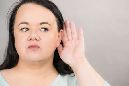 Gossip, rumors and hearing concept. Adult plus size woman round face putting hand to her ear to hear better.の写真素材