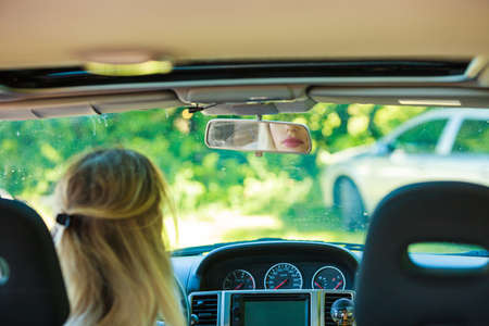 Young blonde woman driving car, view from rear seat