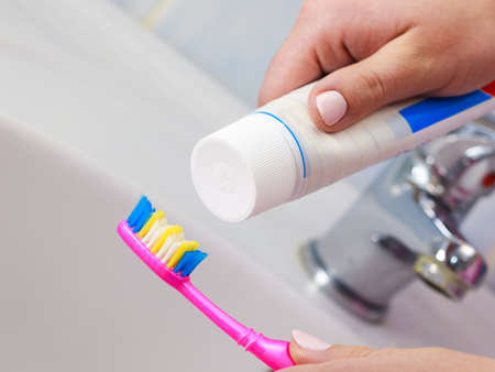 Dental care. Woman hands is holding toothbrush and placing toothpaste on it.