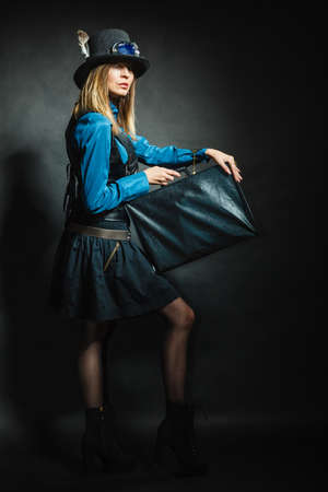 Journey and travel. Retro stylished girl with vintage big bag suitcase valise. Stylish victorian woman on dark background.の写真素材