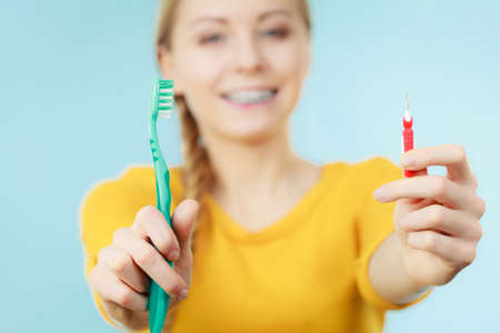 Dentist and orthodontist concept. Young woman with blue braces cleaning and brushing teeth using two different brushes, little interdental brush and manual toothbrushの写真素材