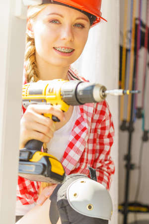 Young woman using drill to fix or installing windows. Girl working at flat remodeling. Building, repair and renovation.の写真素材