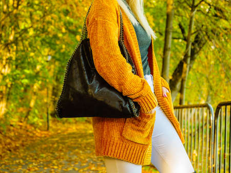 Unrecognizable woman wearing long orange warm cardigan sweater. Autumnal fashion, autumn season styled outfits. Female having a walk in parkの写真素材