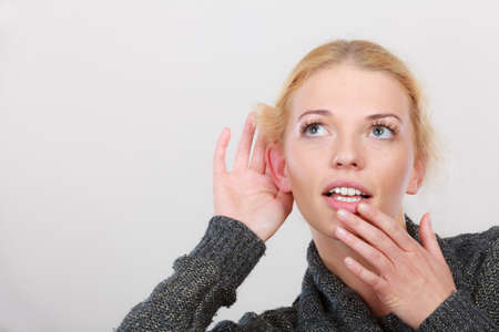 Gestures, gossip and rumors, hearing loss or disorder. Woman put hand to ear for better hear having hand on mouth. Studio shot on light grey backgroungの写真素材