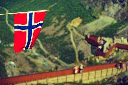 Trollstigen mountain road landscape in Norway, Europe. Norwegian flag waving and many tourists people on viewing platform in background. National tourist route.の写真素材