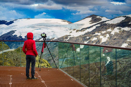 Female tourist with camera on tripod taking travel picture, enjoying mountains landscape from...