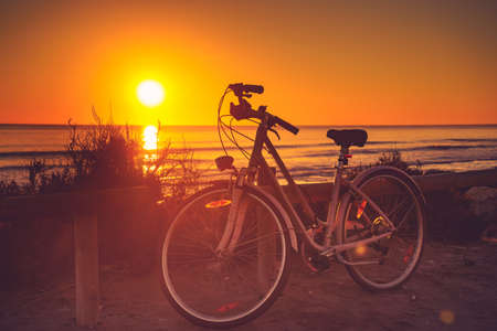 Bicycle outdoor parked on beach, evening time, sunset sky. Holidays, sport and recreation.の写真素材