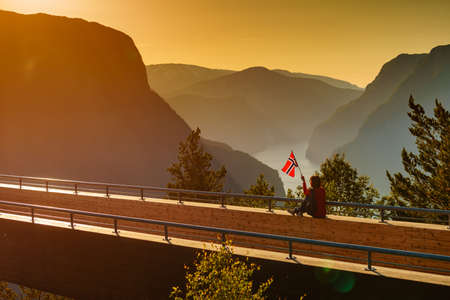 Tourist woman with norwegian flag enjoying fjord Aurlandsfjord view from Stegastein viewing point....
