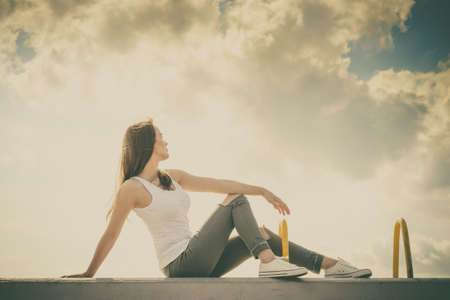 Trendy fashionable woman relaxing outdoor wearing casual footwear white sneakers and hole trousers. Female enjoy sunlight against blue sky.の写真素材