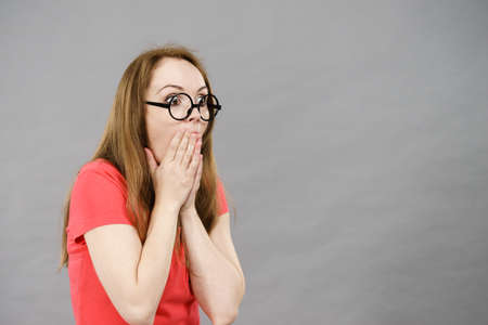 Shocked amazed woman with brown hair wearing funny nerdy rounded black eyeglasses. Studio shot on gray.の写真素材