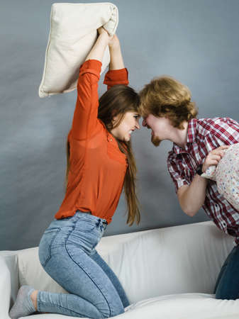 Angry couple having pillow fight. Brother and sister having conflist on sofa.