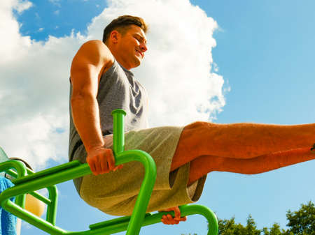 Young man working out in outdoor gym. Sporty guy exercise thigh muscles on street simulators....
