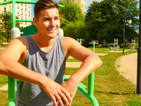 Sportsman relaxing after outdoor workout at street exercise machines for strength exercises. Fit man...