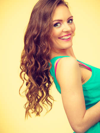 Fashion, hairstyle, beauty concept. Portrait of young, attractive woman with curly brown hair wearing colorful makeup and blue top, indoor shot on yellow backgroundの写真素材