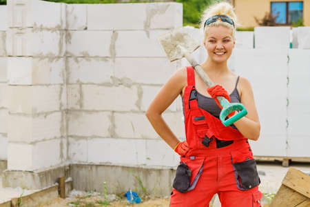 Happy woman worker using shovel standing on industrial construction site, working hard.の写真素材