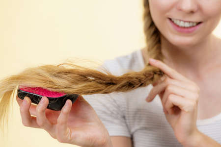 Blonde girl with long braid hair and brush. Girl taking care refreshing her hairstyle. Haircare concept.の写真素材